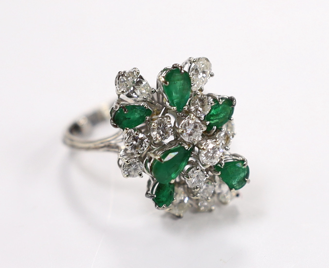 A modern white metal emerald and diamond cluster set dress ring, size R/S, the shank with two sizing spheres, gross weight 8 grams.